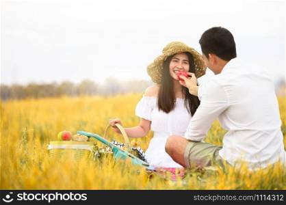 Asian couple doing picnic in golden autumn meadow grass field as honeymoon trip after wedding. Valentines day and family love concept. Outdoors nature and long vacation relaxation. People lifestyes