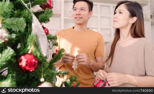 Asian couple feeling happy decorating christmas tree in their living room at home in Christmas Festival. Lifestyle woman and man happy celebrate summer christmas and New year concept.