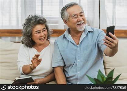 Asian couple Grandparent taking Video call to grandchild or taling selfie with happy feeling by mobile phone in house, Long live and Elderly society,Warm family and happiness,social distancing concept