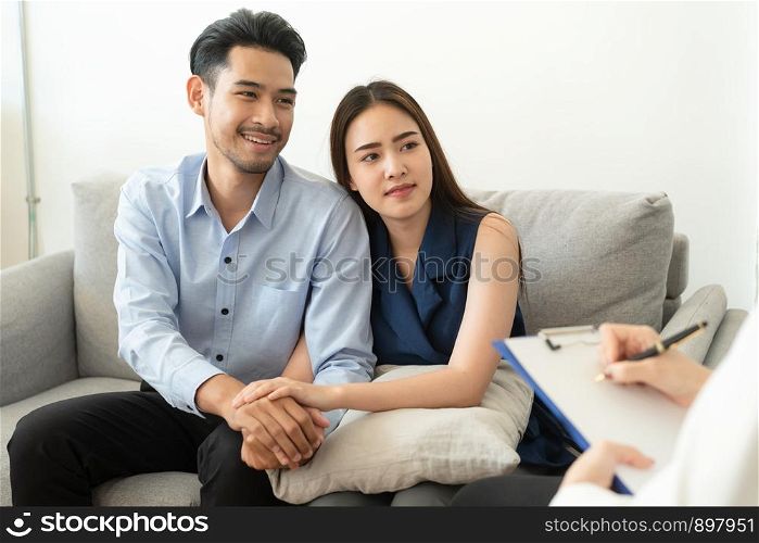 Asian couple join hand to encourage while sitting on the couch in the psychiatrist room to consult mental health problems by doctor, Health and illness concepts