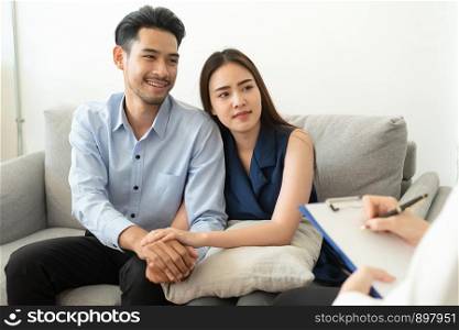 Asian couple join hand to encourage while sitting on the couch in the psychiatrist room to consult mental health problems by doctor, Health and illness concepts