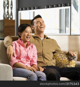 Asian couple laughing while watching television.
