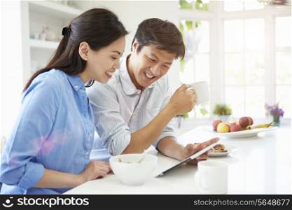 Asian Couple Looking At Digital Tablet Over Breakfast