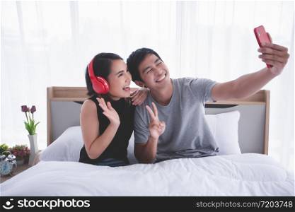 Asian couple lovers lying on their play mobile phones and selfie on bed at home