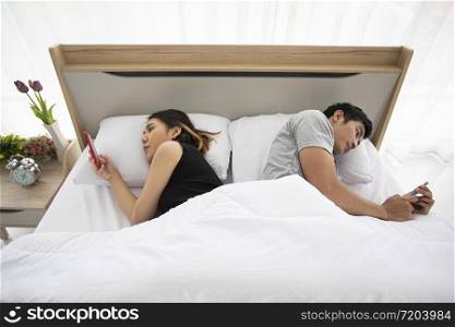 Asian couple lovers lying on their play mobile phones on bed