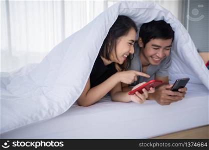 Asian couple lovers lying on their play mobile phones on bed at home