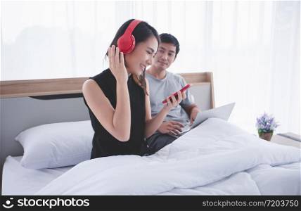 Asian couple lovers put on headphones for listening to music and singing on his bed and happy on relax time at home