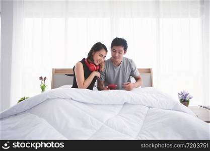 Asian couple lovers put on headphones for listening to music and singing on his bed and happy on relax time at home