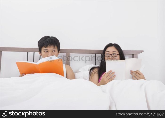 Asian couple reading books while looking at each other in bed
