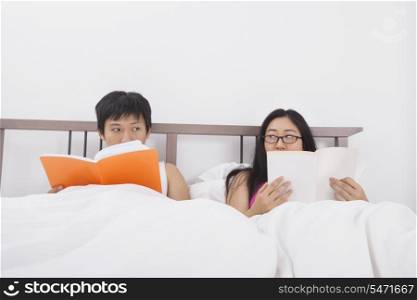 Asian couple reading books while looking at each other in bed