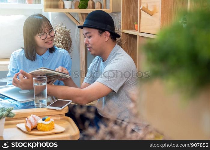 Asian couple reading the magazine over the desk which have technology laptopn in modern workplace or co-working space, freelance and lifestyle or leisure concept