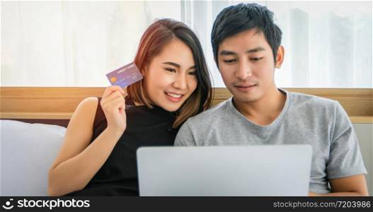 Asian Couple shopping online and paying with credit card at laptop computer,Happy couple at home surfing the net in bed