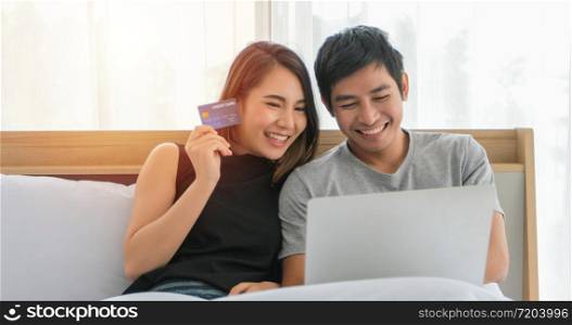 Asian Couple shopping online and paying with credit card at laptop computer,Happy couple at home surfing the net in bed