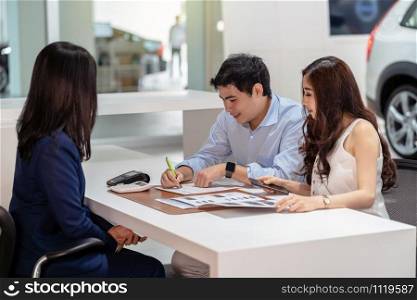 Asian couple signing the contract with saleswoman after decision the buy the new car in showroom, Customer service and sales representative concept