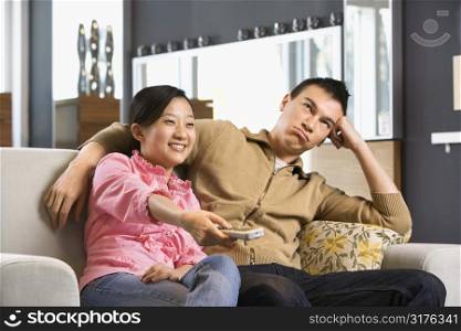 Asian couple sitting on couch watching TV.