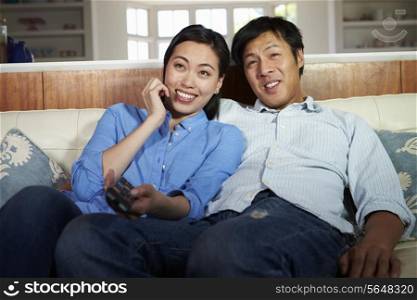 Asian Couple Sitting On Sofa Watching TV Together