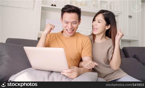 Asian couple using laptop for search web in living room at home, sweet couple enjoy love moment while lying on the sofa when relax at home. Lifestyle couple relax at home concept.