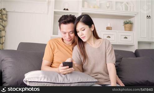 Asian couple using smartphone check social media in living room at home, sweet couple enjoy love moment while lying on the sofa when relax at home. Lifestyle couple relax at home concept.