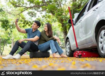 Asian couple using smartphone for assistance after a car breakdown on street. Concept of vehicle engine problem or accident and emergency help from Professional mechanic