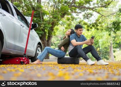 Asian couple using smartphone for assistance after a car breakdown on street. Concept of vehicle engine problem or accident and emergency help from Professional mechanic