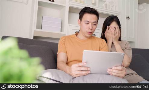 Asian couple using tablet for online shopping in internet in living room at home, sweet couple enjoy love moment while lying on the sofa when relax at home. Lifestyle couple relax at home concept.