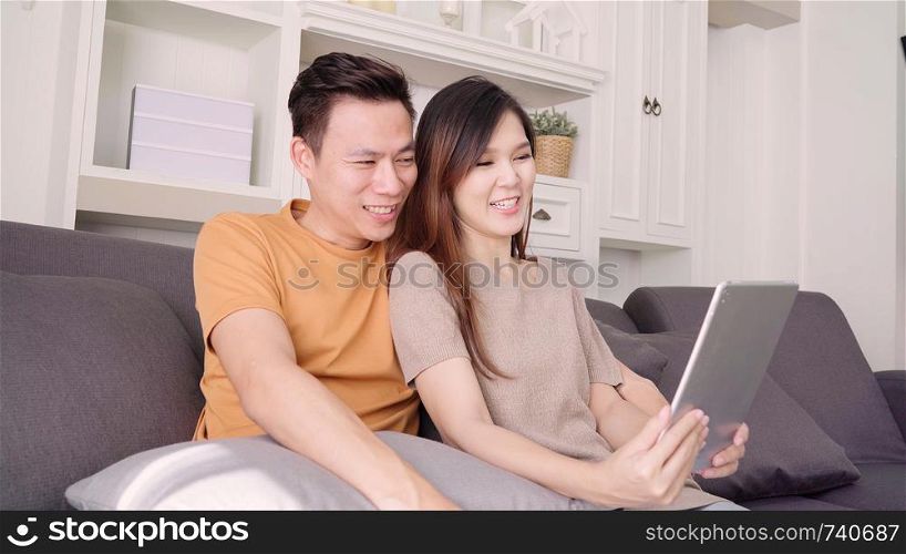Asian couple using tablet VIDEO Call with friend in living room at home, sweet couple enjoy love moment while lying on the sofa when relaxed at home. Lifestyle couple relax at home concept.
