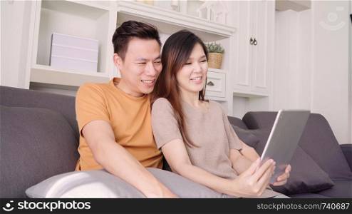 Asian couple using tablet VIDEO Call with friend in living room at home, sweet couple enjoy love moment while lying on the sofa when relaxed at home. Lifestyle couple relax at home concept.