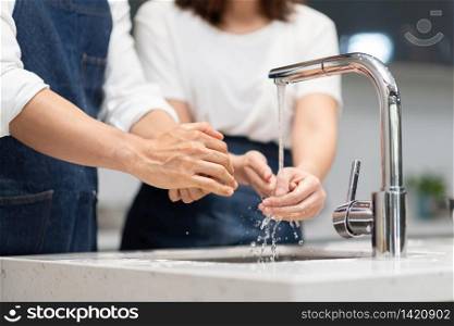 Asian couple washing hands with foam soap before cooking at home. Man and woman cleaning and rubbing nails and fingers with water at sink in kitchen. Hygiene, preventing coronavirus.