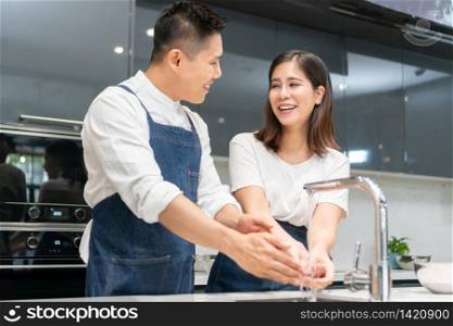 Asian couple washing hands with foam soap before cooking together. Happy smiling Young Man and woman cleaning and rubbing nails and fingers with water at sink in kitchen. Hygiene, preventing coronavirus.