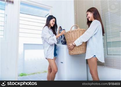 Asian couple women doing housework and chores in front of washing machine and loading clothes and in laundry room together. People and daily life concept. Friendship and Lesbian theme.