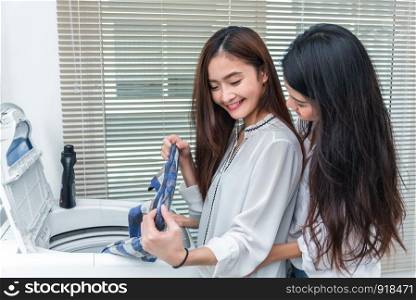 Asian couple women doing housework and chores in front of washing machine and loading clothes in laundry room together. People and daily life concept. Friendship and Lesbian theme. LGBT pride theme