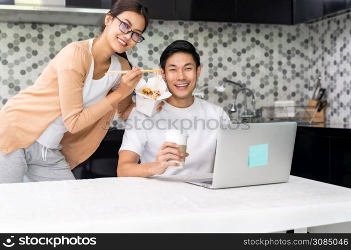 Asian couple work from home in the kitchen and eating delivery chinese take away food and take out coffee while city lockdown from coronavirus covid-19 pandemic. New Normal lifestyle working from home.