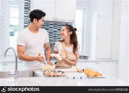 Asian couples cooking and baking cake together in kitchen room. Man and woman looking to each other at home. Love and happiness concept Sweet honeymoon and Valentine day theme