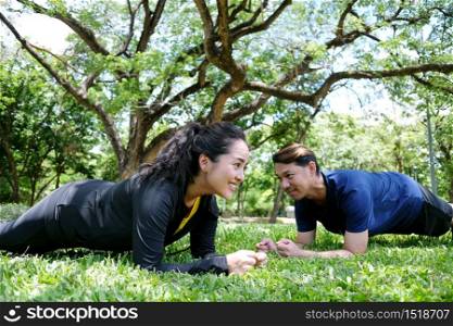 Asian couples exercising and planking workout together on grass field in the garden. Social distancing and new normal life Concept