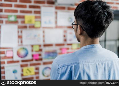 Asian creative man drawing work plan on paper board. Young professional business male think and write information reminder on paper on brick, business situation, startup in Loft office concept.