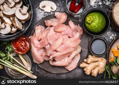 Asian cuisine, cooking ingredients with raw sliced chicken breast, lime, chili sauce, lemon grass, ginger, vegetables and mushrooms, top view