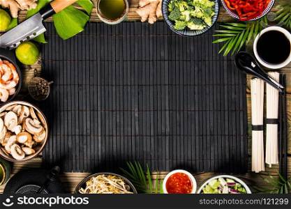 Asian cuisine ingredients on bamboo mat over old wooden background, top view. Vegetables, spices, shrimp, noodles, sauces for cooking vietnamese, thai or chinese food. Clean eating food concept