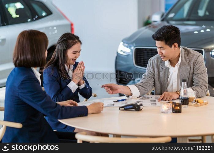 Asian customer giving the credit card to sales representative for purchase new car after sign contract and agreement in the showroom, Customer service and sales car concept