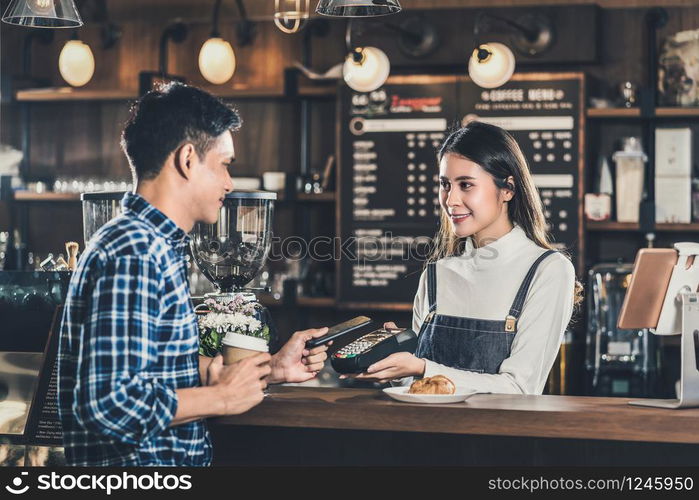 Asian customer man paying via contactless channel by mobile banking application to Asian Small business owner at the table in coffee shop, Small business owner and startup in coffee shop concept