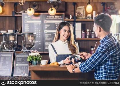 Asian customer man paying with credit card via contactless nfs technology to Asian Barista of Small business owner at the table in coffee shop, Small business owner and startup in coffee shop concept