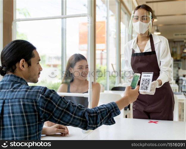 Asian customer scan QR code online menu from waitress with face mask and face shield. Customer sat on social distancing table for new normal lifstyle in restaurant after coronavirus covid-19 pamdemic.