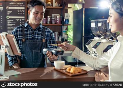 Asian customer using her credit card with contactless nfs technology to pay a barista for her coffee purchase at a cafe bar.