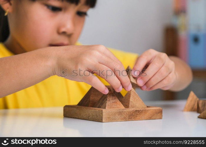 Asian cute little girl playing with wooden toy jigsaw puzzle pyramid on table. Healthy children training memory and thinking. Wooden puzzles are games that increase intelligence for children. Educational toys for children.