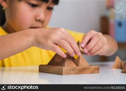 Asian cute little girl playing with wooden toy jigsaw puzzle pyramid on table. Healthy children training memory and thinking. Wooden puzzles are games that increase intelligence for children. Educational toys for children.