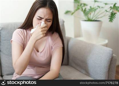 Asian Cute of girl having flu season adn sneeze using paper tissues sitting on sofa at home, Health and illness concepts