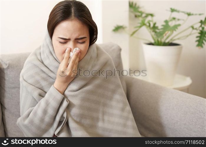 Asian Cute of girl having flu season and sneeze using paper tissues sitting on sofa at home, Putting blanket, Health and illness concepts