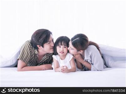 Asian dad and mom are kissing their daughter while staying on bed in the morning