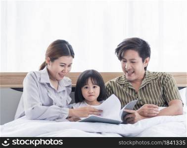 Asian dad and mom are reading bedtime stories to their daughter before sleeping