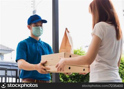 Asian delivery express courier young man giving paper bags fast food and pizza box to woman customer receiving both protective face mask, under curfew quarantine pandemic coronavirus COVID-19