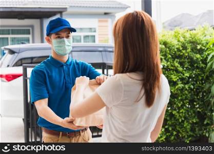 Asian delivery express courier young man giving paper bags fast food to woman customer receiving both protective face mask, under curfew quarantine pandemic coronavirus COVID-19